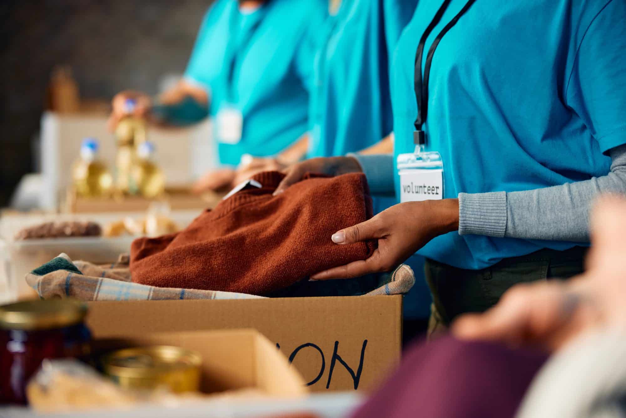 Volunteers in turquoise T-shirts and lanyards sorting folded clothes into a cardboard donation box